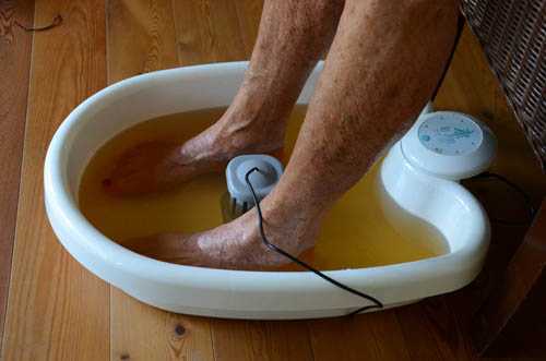 Zwei Beine stehen in einem Fußbad mit braunem Wasser